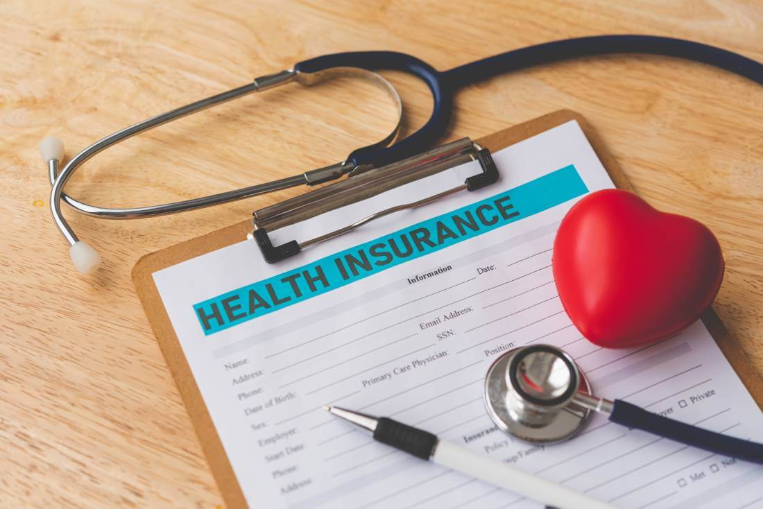 Health Insurance Form on a clipboard, near pen, stethoscope, and foam heart.
