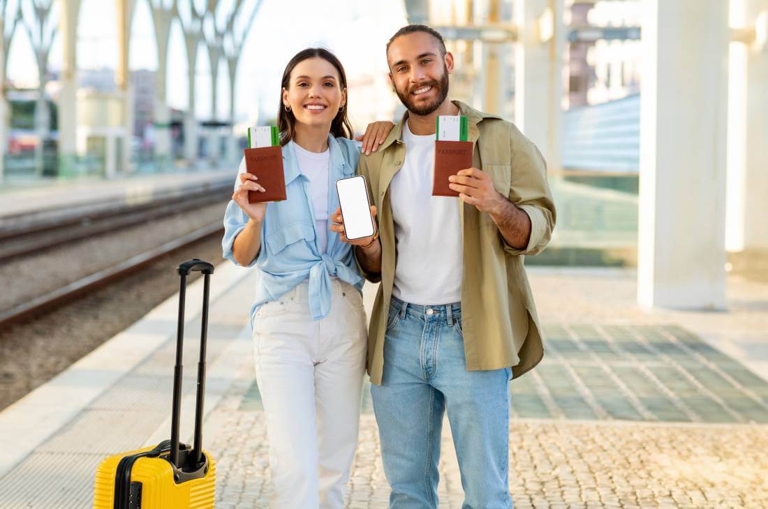 A man and woman with their luggage hold up their passports an plane tickets.